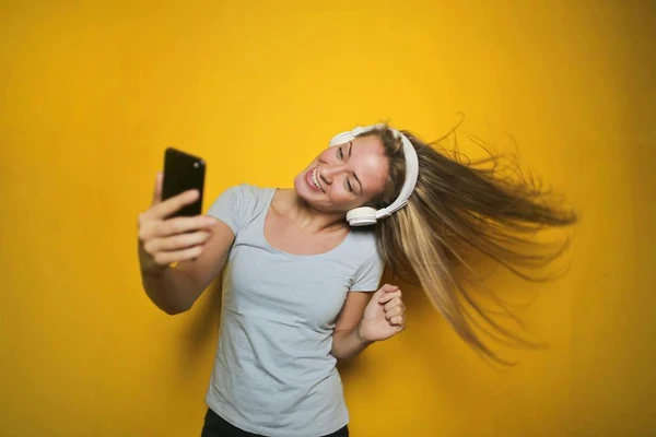 A girl rocks out in her headphones while looking at her phone against a yellow background