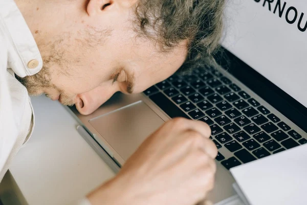 A man is exhausted at work and falls asleep face down on his computer