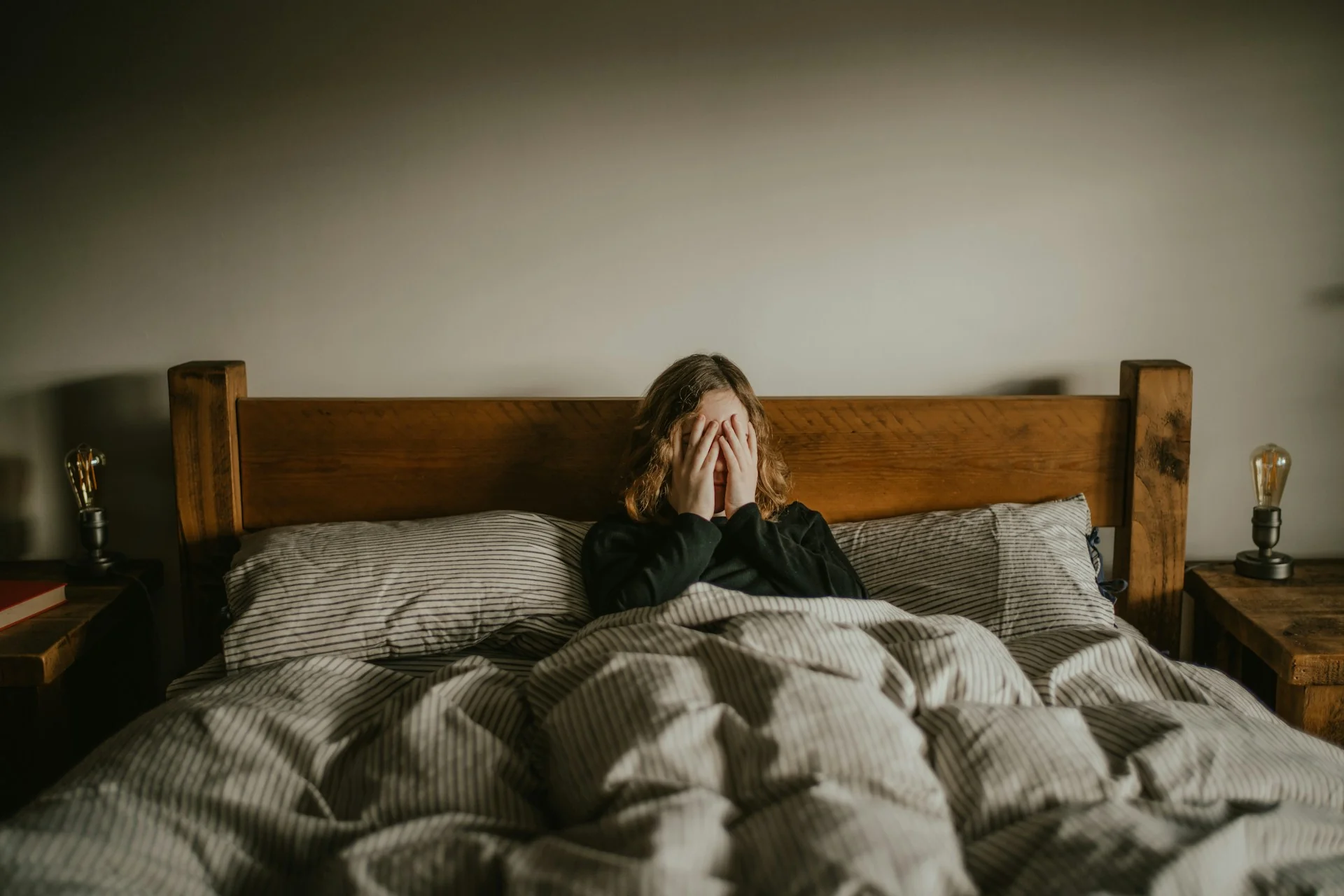 A woman covers her face with her hands, looking sad, while wrapped up in bed