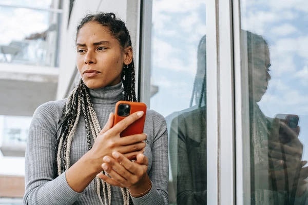 A lady gets FOMO while looking at her social media apps on her phone and gazes out into the distance depressed