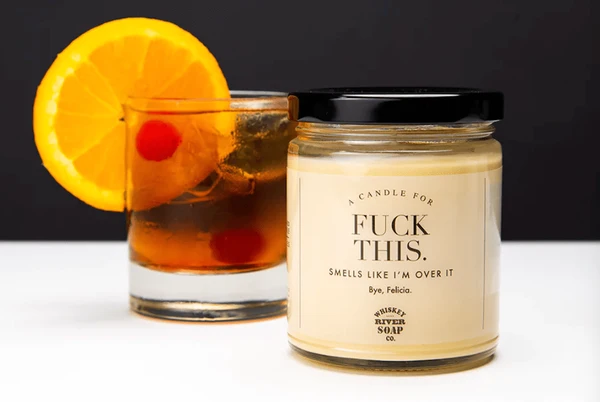 A candle labeled "FUCK THIS." next to a whiskey old fashioned