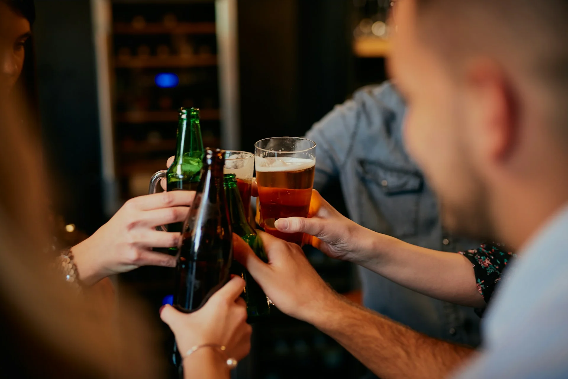 A group of friends cheers their alcoholic drinks while out at a bar