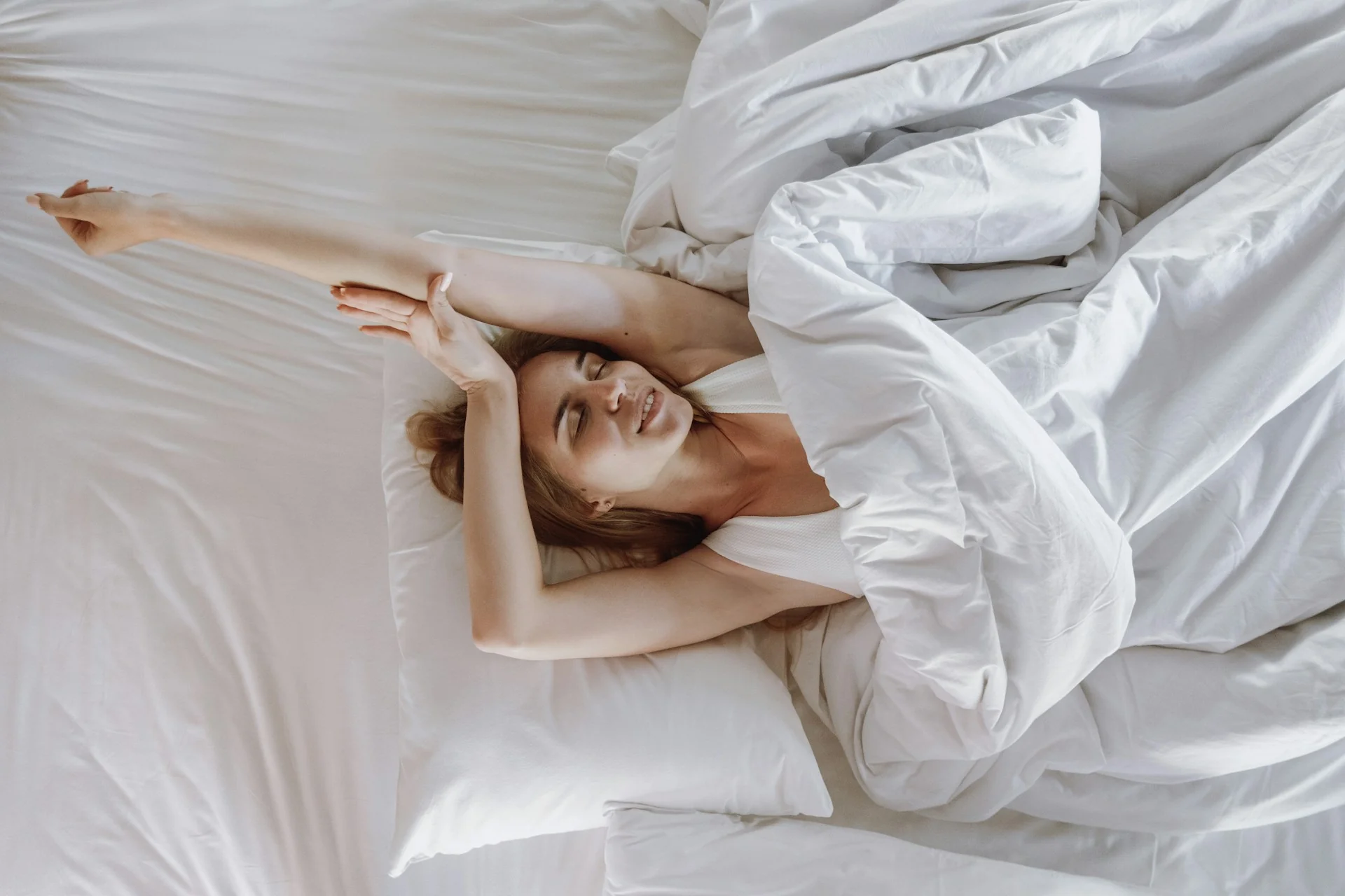A woman smiles while stretching in bed after a good night's sleep