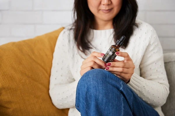 An Asian lady is sitting on her office couch holding a bottle of Sunday Scaries CBD Oil