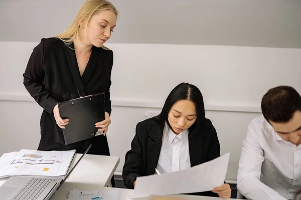 A micromanaging boss hovers over her employees during a meeting