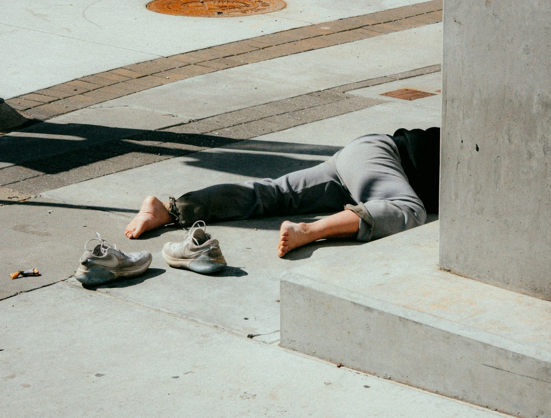 Person lying barefoot on a concrete ledge after overdoing THC, with shoes left on the pavement nearby