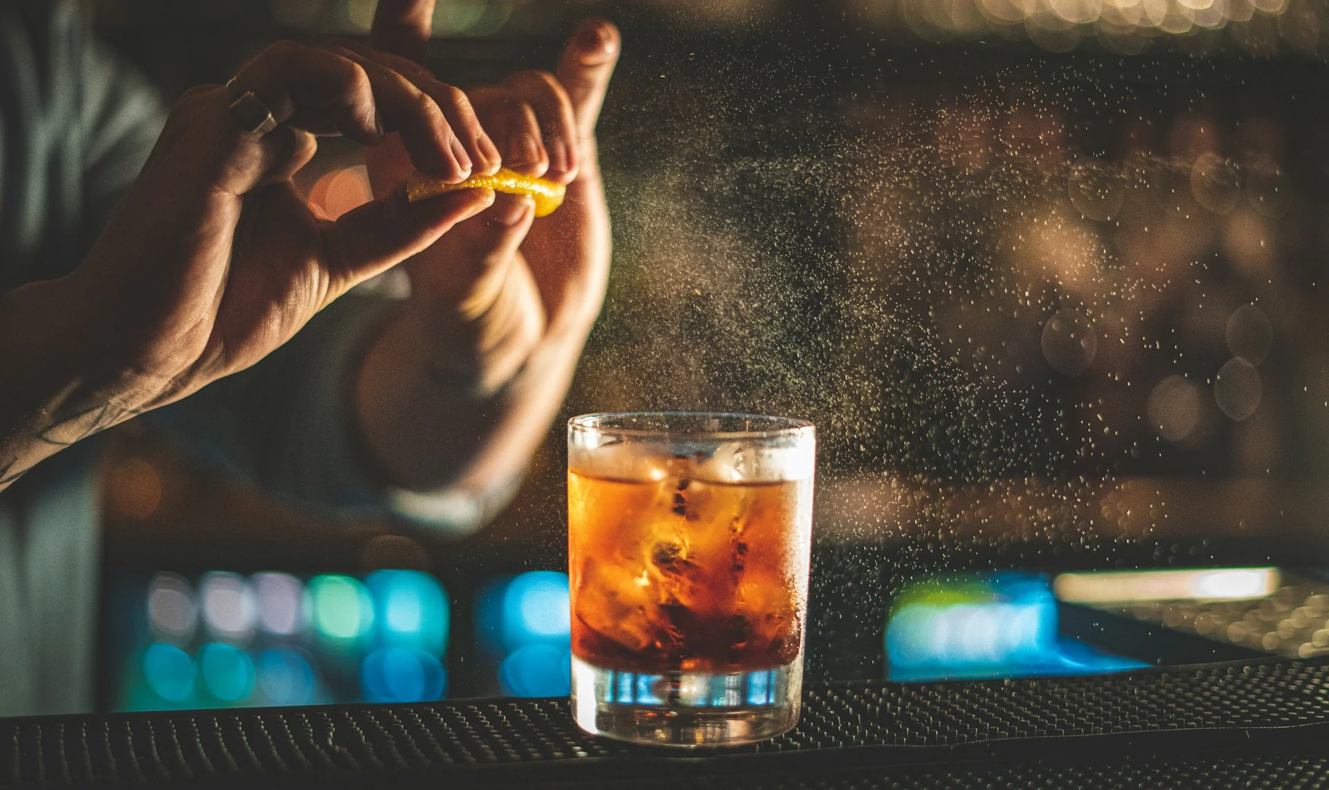 A bartender squeezes an orange over an alcoholic drink on a bar