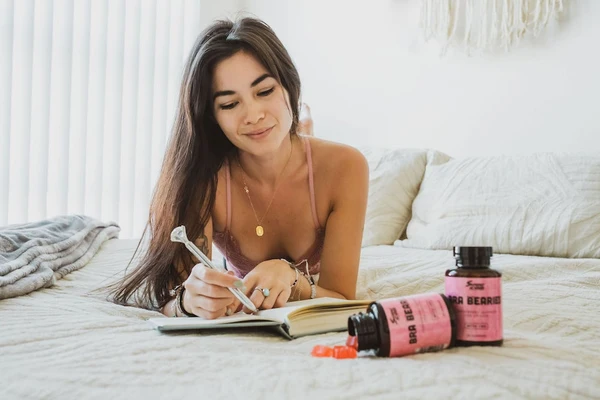 A woman lies on her bed and sets her weekend intentions by writing in her journal