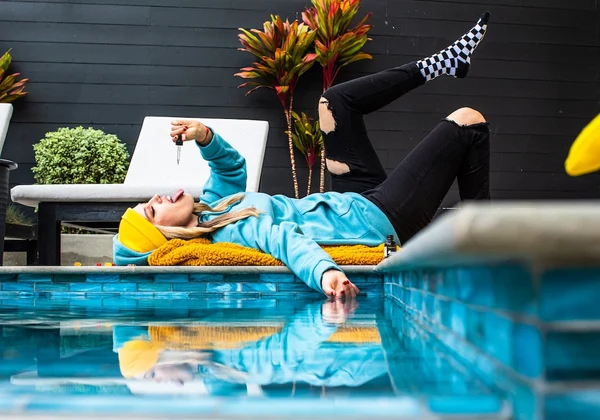 A depressed and hungover girl lays on her back by the pool putting Sunday Scaries stress relief oil in her mouth