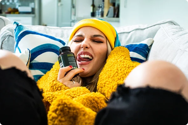A woman in a yellow beanie curled up on the couch with the Sunday Scaries
