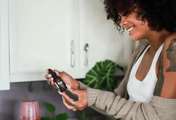 A happy woman holds a bottle of Sunday Scaries CBD oil in front of her cabinet