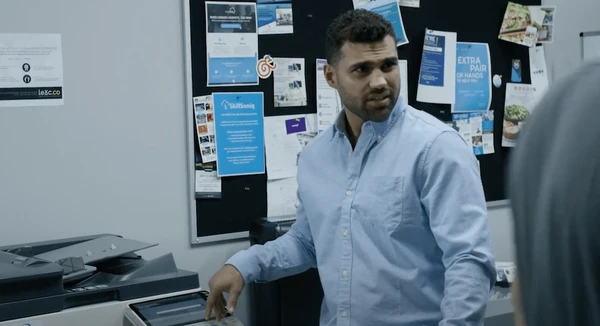A man at his office is visibly annoyed while standing next to the copier machine
