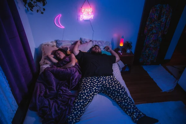 A couple is sound asleep while the man sprawls out and takes over most of the bed