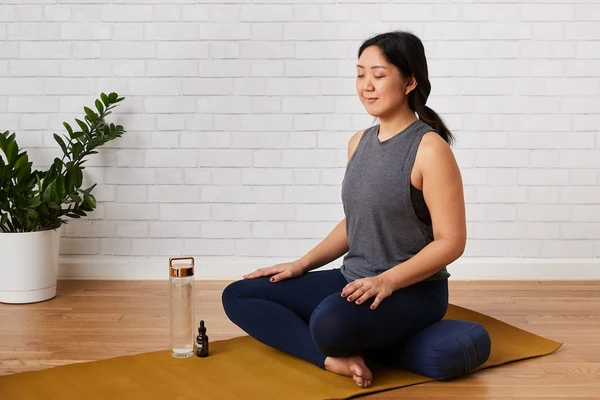A woman meditates at work on her yoga mat with a bottle of water and Sunday Scaries CBD Oil