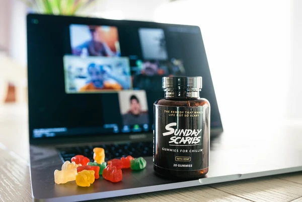 A bottle of Sunday Scaries CBD gummies sits on an Apple MacBook with a Zoom call on the screen