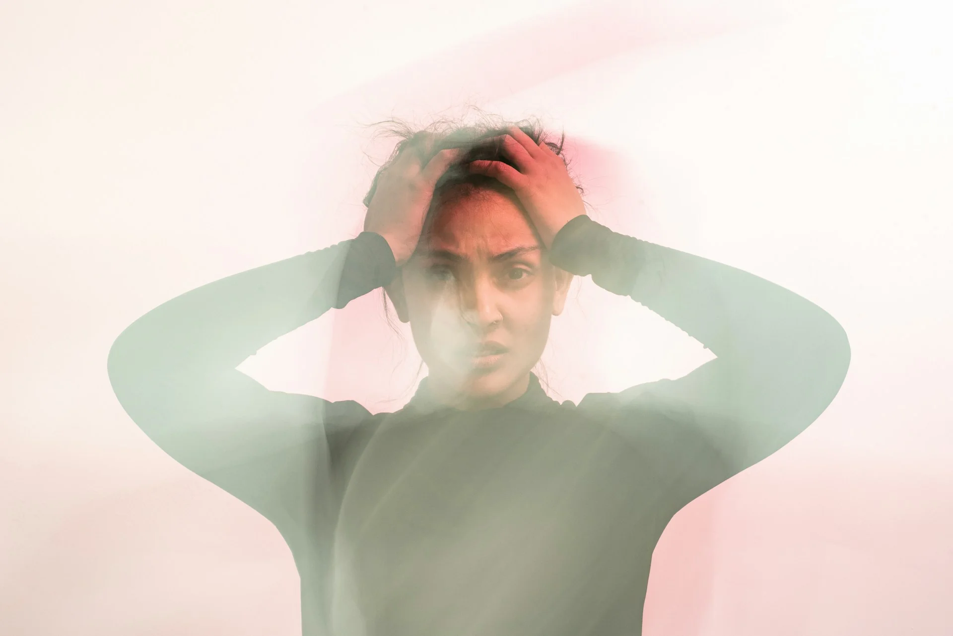 A woman holds her head, with blur across the image, representing anxious, lost feelings
