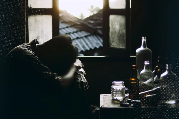 An image of a man in a dark room surrounded by alcohol bottles to reveal how to understand Hangxiety