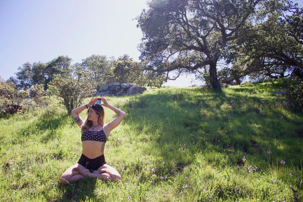 A woman holding a bottle of vegan CBD gummies meditates in a meadow