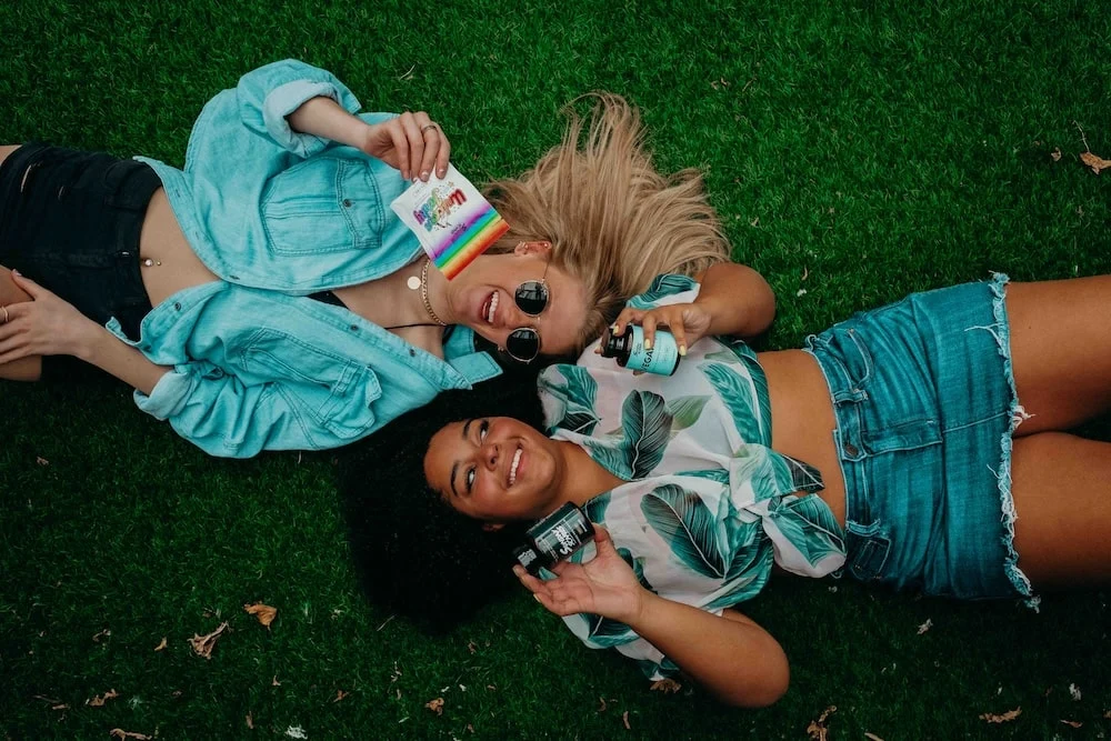 Two ladies lay down on the ground with cannabis products showing the difference between CBD vs CBN