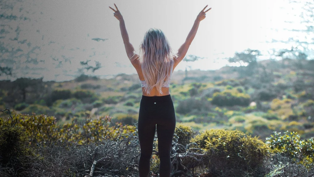 A woman free from migraines admires the view with her hands in the air 
