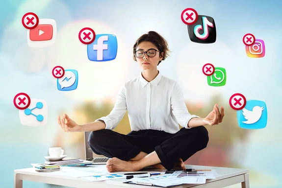 A woman meditates in lotus pose on her desk with her eyes closed while a bunch of x'd out social media apps fly around her