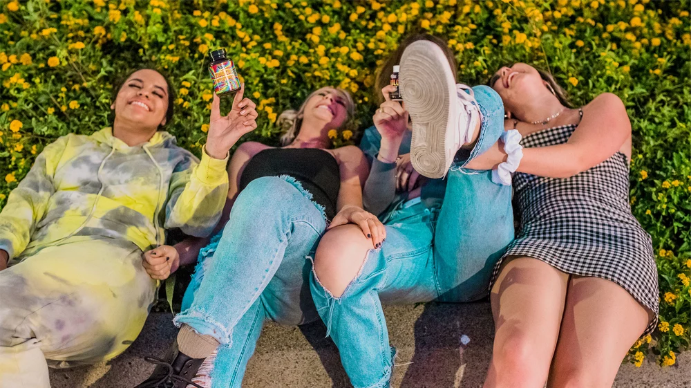 A group of girls lay on the grass laughing holding up a bottle to show what delta-9 gummies are