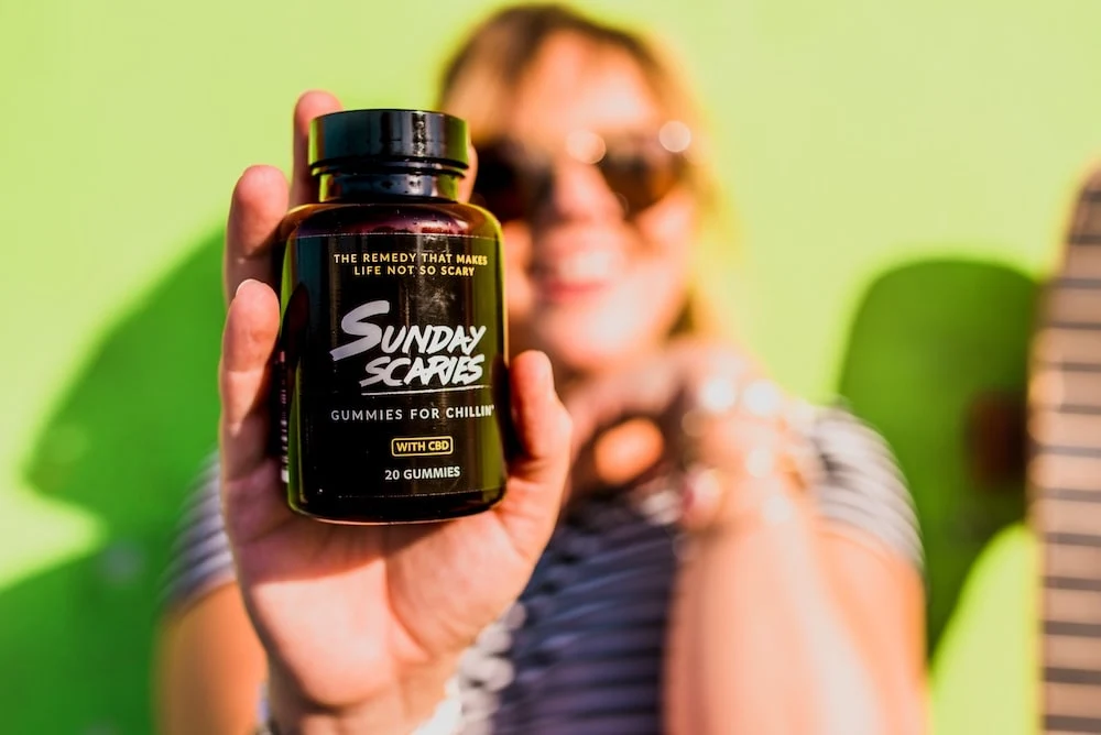 A woman holds up a bottle of Sunday Scaries while smiling, showing what CBD gummies do. 