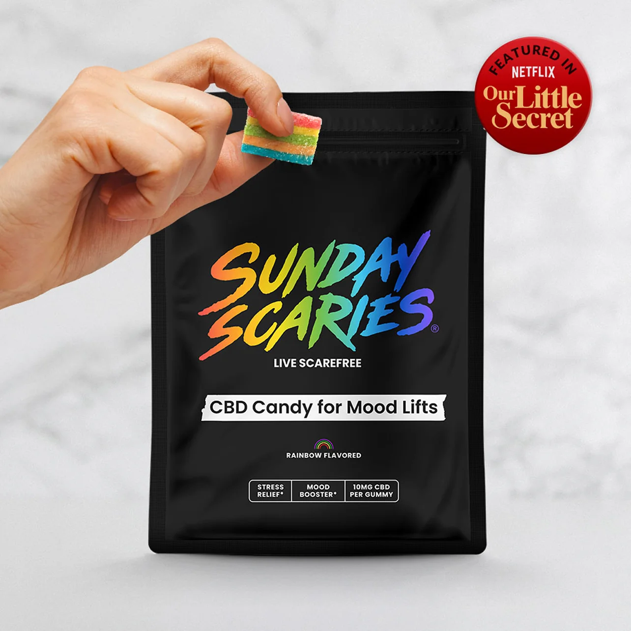 Black bag labeled 'Sunday Scaries' with colorful text, a hand holding a gummy candy and a badge showing it was featured in the Netflix movie 