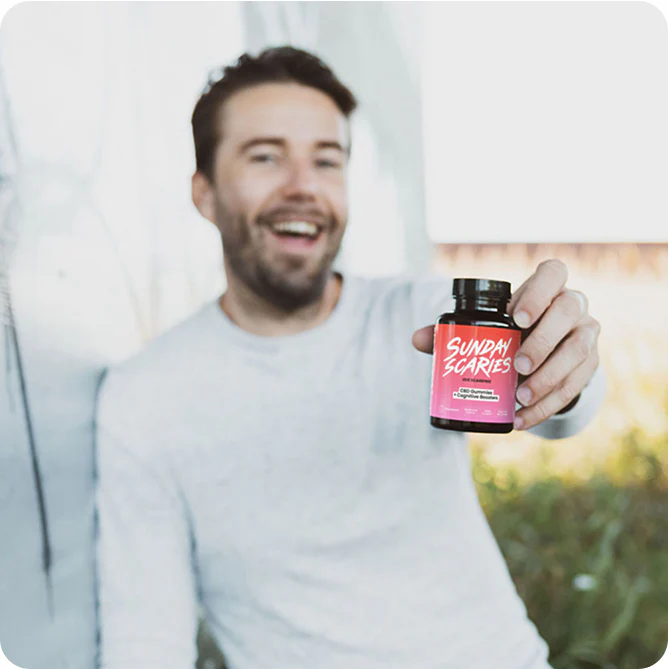 A man in a white shirt holds out a bottle of Sunday Scaries focus edition gummies