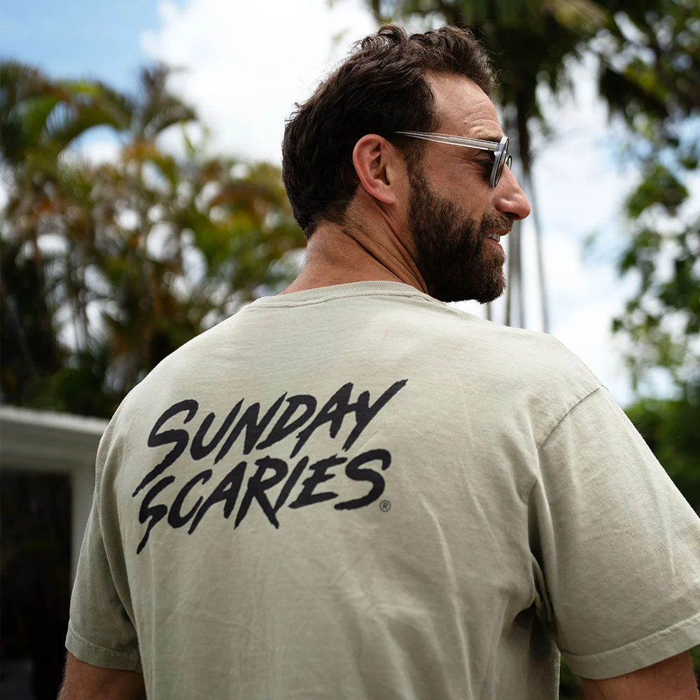 A man shows off the back of his sunday scaries pocket tee