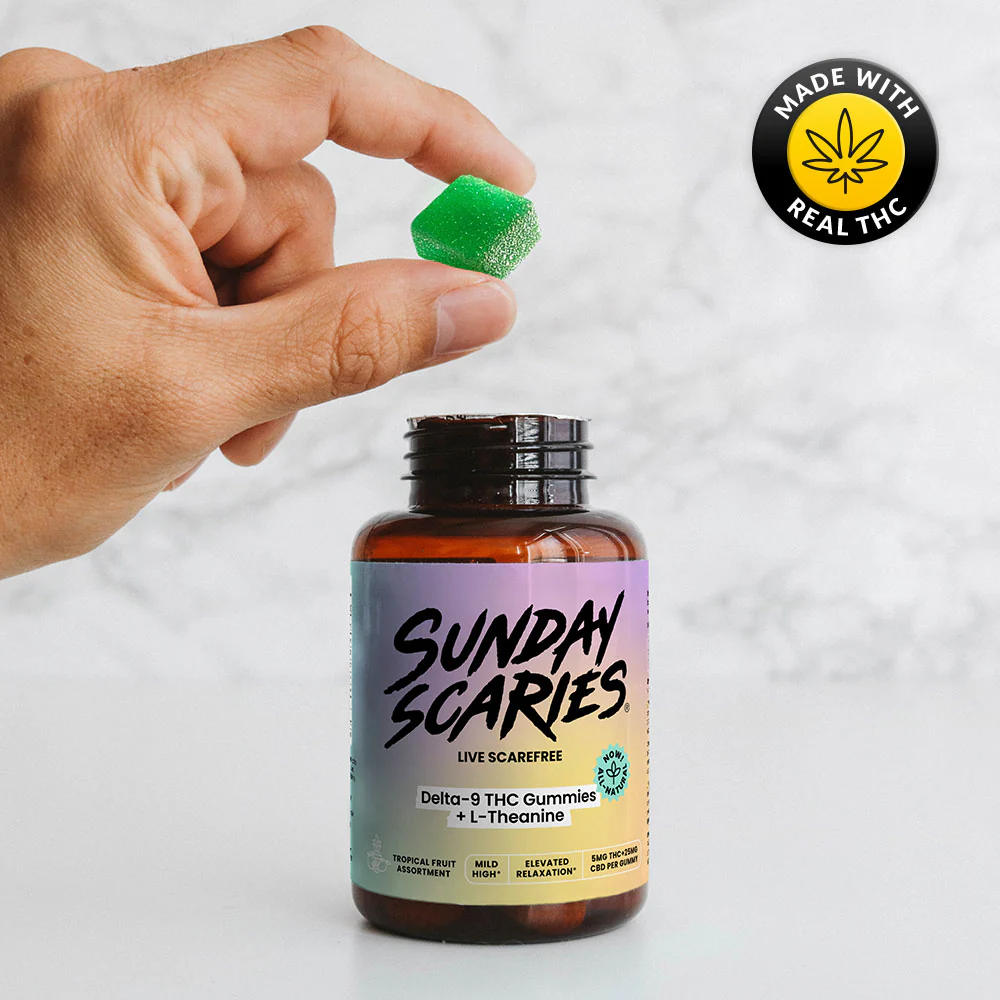 A hand holding an orange THC gummy with a Sunday Scaries delta-9 gummies and a 