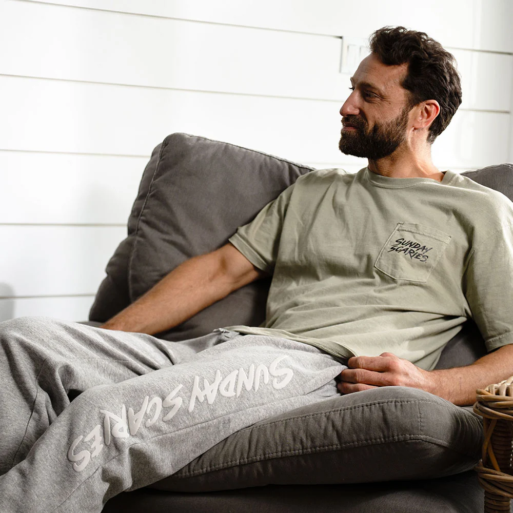 A man wears the Sunday Scaries sweatpants on his chair