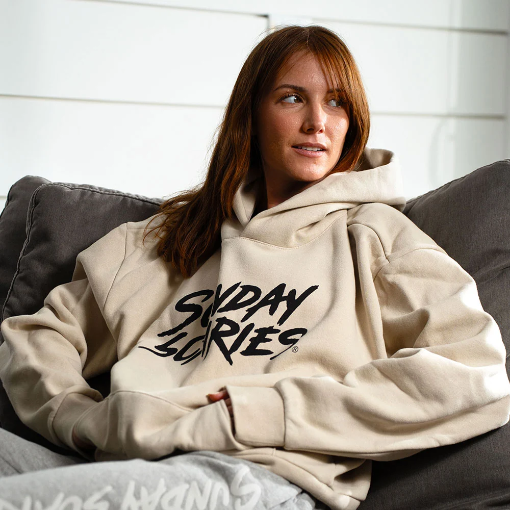 A red hair woman wears the Sunday Scaries sweatshirt in her living room
